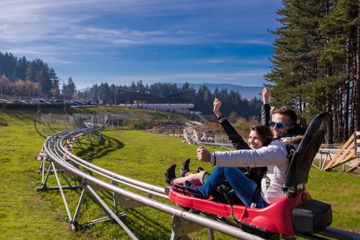 Excited young couple driving alpine coaster while enjoying beautiful sunny day in the nature