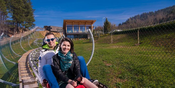 Excited young couple driving alpine coaster while enjoying beautiful sunny day in the nature