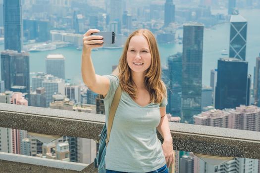 Hong Kong Victoria Peak woman taking selfie stick picture photo with smartphone enjoying view over Victoria Harbour. Viewing platform on top of Peak Tower, HK. Defocused background.Travel asia concept.