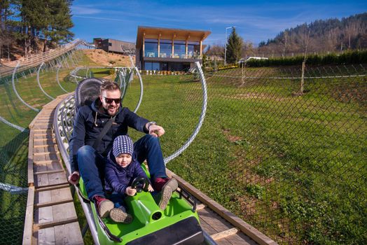 Excited young father and son driving on alpine coaster while enjoying beautiful sunny day in the nature