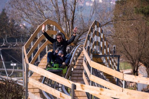 Excited young father and son driving on alpine coaster while enjoying beautiful sunny day in the nature