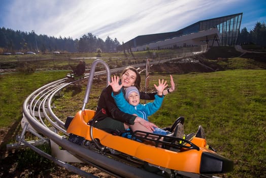 Excited young mother and son driving on alpine coaster while enjoying beautiful sunny day in the nature