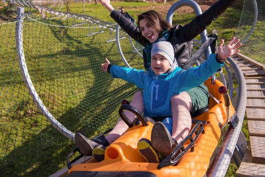 Excited young mother and son driving on alpine coaster while enjoying beautiful sunny day in the nature