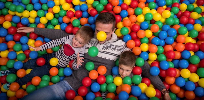 happy family enjoying free time young dad and kids playing in pool with colorful balls at childrens playroom