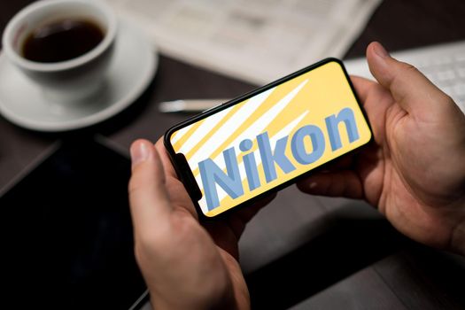 New York, New York / USA - 11 11 2019: Logo of Nikon on the iPhone X in hands in office