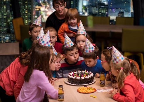 young happy boy and group of his friends having birthday party with a night city through the windows in the background