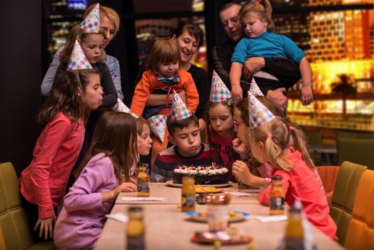 young happy boy and group of his friends having birthday party with a night city through the windows in the background