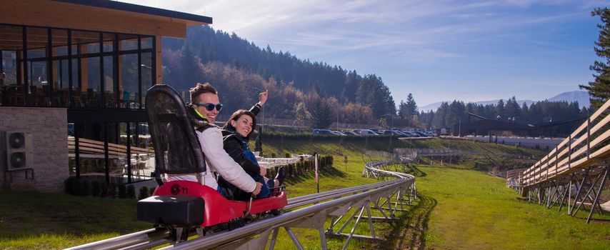 Excited young couple driving alpine coaster while enjoying beautiful sunny day in the nature