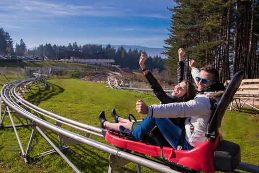 Excited young couple driving alpine coaster while enjoying beautiful sunny day in the nature