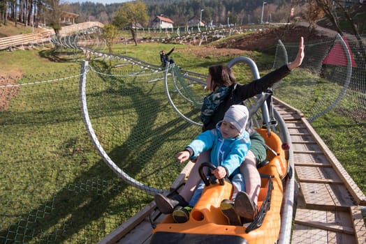 young excited mother and son enjoys driving on alpine coaster