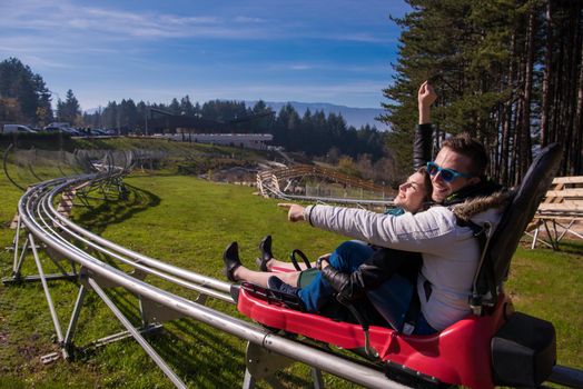 Excited young couple driving alpine coaster while enjoying beautiful sunny day in the nature