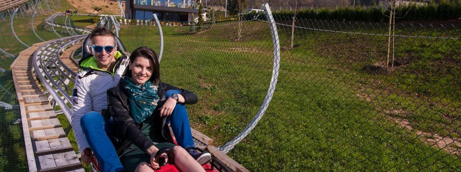 Excited young couple driving alpine coaster while enjoying beautiful sunny day in the nature