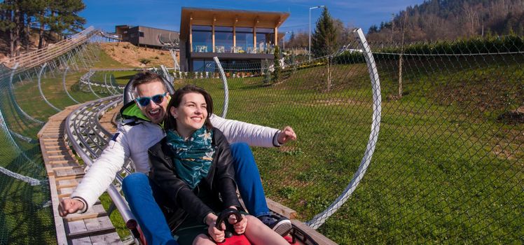 Excited young couple driving alpine coaster while enjoying beautiful sunny day in the nature