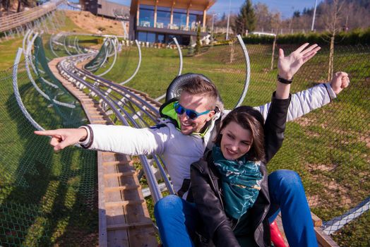 Excited young couple driving alpine coaster while enjoying beautiful sunny day in the nature