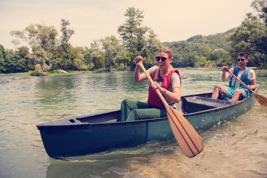 Couple adventurous explorer friends are canoeing in a wild river surrounded by the  beautiful nature