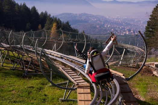 Excited young couple driving alpine coaster while enjoying beautiful sunny day in the nature