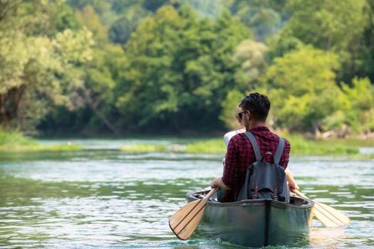 Couple adventurous explorer friends are canoeing in a wild river surrounded by the  beautiful nature