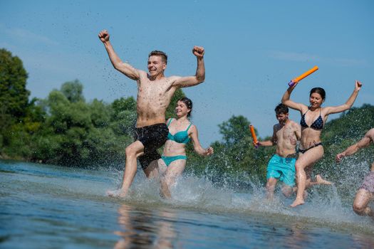 summer joy group of happy friends having  fun while running and splashing on river