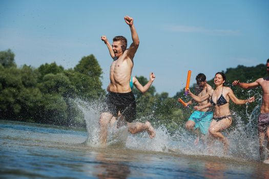 summer joy group of happy friends having  fun while running and splashing on river