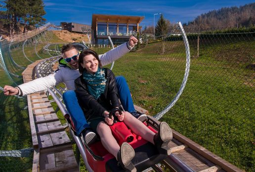 Excited young couple driving alpine coaster while enjoying beautiful sunny day in the nature