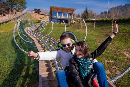 Excited young couple driving alpine coaster while enjoying beautiful sunny day in the nature