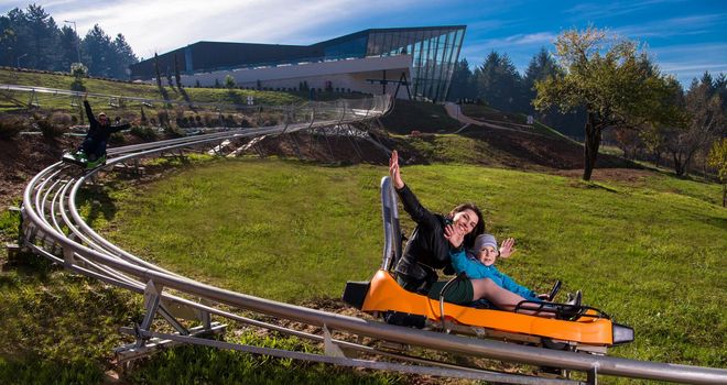 Excited young mother and son driving on alpine coaster while enjoying beautiful sunny day in the nature