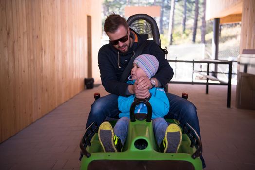 Excited young father and son driving on alpine coaster while enjoying beautiful sunny day in the nature