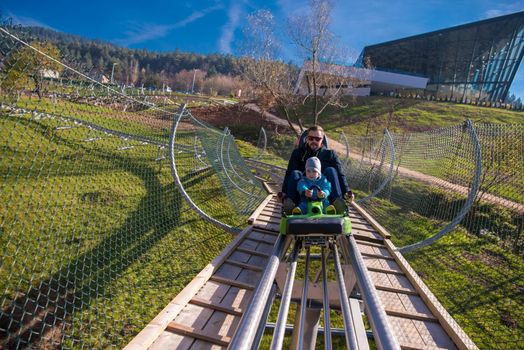 Excited young father and son driving on alpine coaster while enjoying beautiful sunny day in the nature