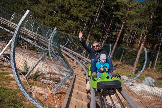 Excited young father and son driving on alpine coaster while enjoying beautiful sunny day in the nature