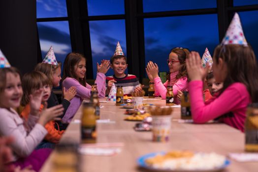 young happy boy and group of his friends having birthday party with a night sky through the windows in the background