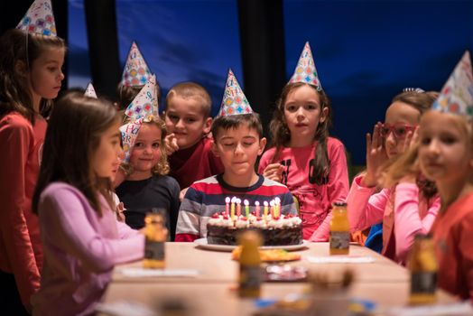 young happy boy and group of his friends having birthday party with a night sky through the windows in the background