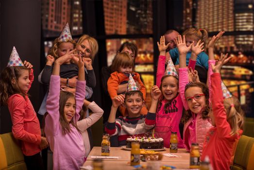 young happy boy and group of his friends having birthday party with a night city through the windows in the background