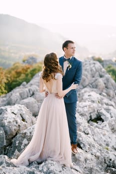 Groom hugs bride by the waist on a rocky mountain. High quality photo