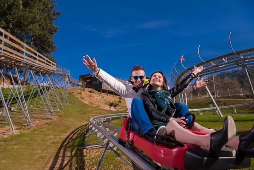 Excited young couple driving alpine coaster while enjoying beautiful sunny day in the nature