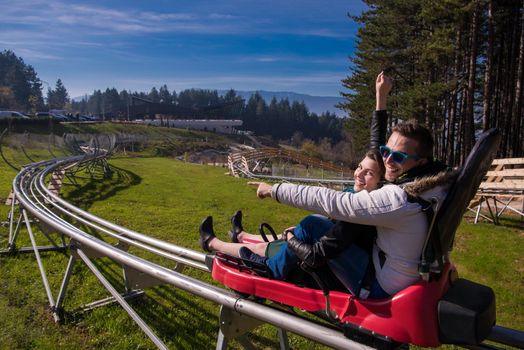 Excited young couple driving alpine coaster while enjoying beautiful sunny day in the nature