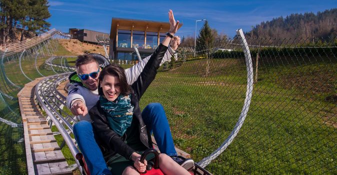 Excited young couple driving alpine coaster while enjoying beautiful sunny day in the nature