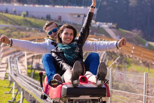 Excited young couple driving alpine coaster while enjoying beautiful sunny day in the nature