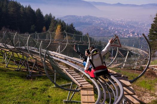 Excited young couple driving alpine coaster while enjoying beautiful sunny day in the nature