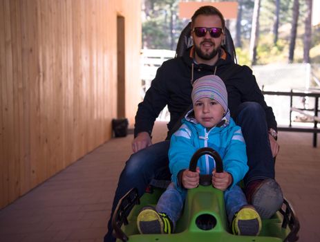 Excited young father and son driving on alpine coaster while enjoying beautiful sunny day in the nature