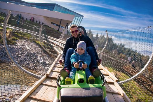 Excited young father and son driving on alpine coaster while enjoying beautiful sunny day in the nature