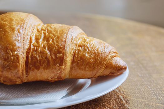 Fresh croissant on a white plate on a wooden table