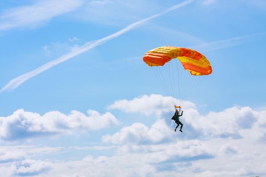 Skutech, Czech Republic, 6 August 2020: A parachutist with an orange parachute canopy against a background of blue sky and white clouds. Skydiving.