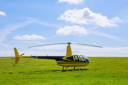 Modern light yellow helicopter on a grassy field against the blue sky.