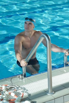 Happy muscular swimmer wearing glasses and cap at swimming pool and represent health and fit concept