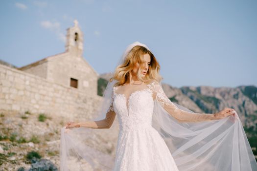 Bride in a white lace dress stands against the background of an ancient stone church. High quality photo