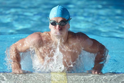 Happy muscular swimmer wearing glasses and cap at swimming pool and represent health and fit concept