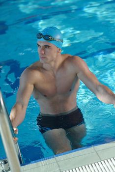 Happy muscular swimmer wearing glasses and cap at swimming pool and represent health and fit concept