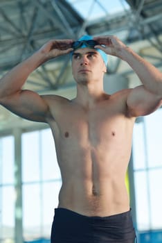 Happy muscular swimmer wearing glasses and cap at swimming pool and represent health and fit concept