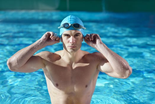 Happy muscular swimmer wearing glasses and cap at swimming pool and represent health and fit concept