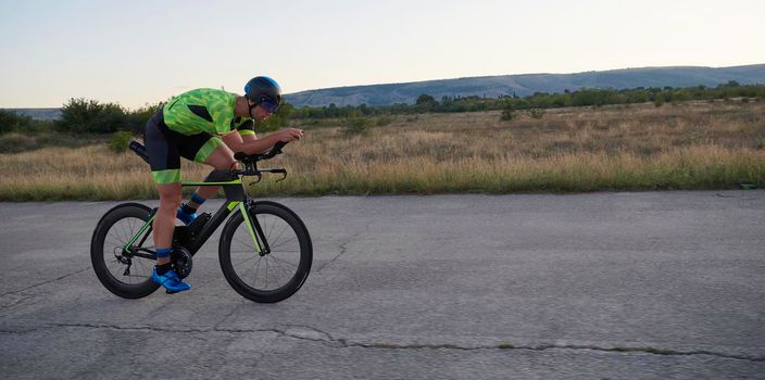 triathlon athlete riding professional racing bike on morning workout sunset or sunrise in background